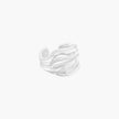 Wide sterling silver cuff ring with flowing wave patterns creating dimensional texture against cream background