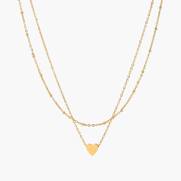 Delicate double-chain gold necklace with tiny heart pendant on cream background