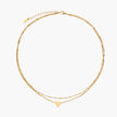 Delicate double-chain gold necklace with tiny heart pendant on cream background