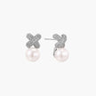 White gold plated studs featuring pavé X-shaped tops with freshwater pearl drops on cream background.