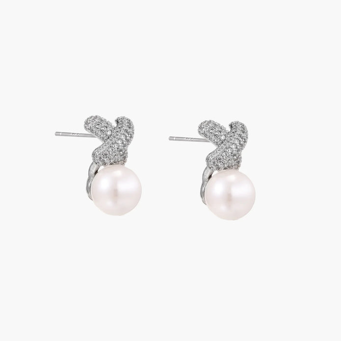 White gold plated studs featuring pavé X-shaped tops with freshwater pearl drops on cream background.