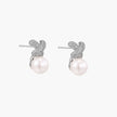 White gold plated studs featuring pavé X-shaped tops with freshwater pearl drops on cream background.