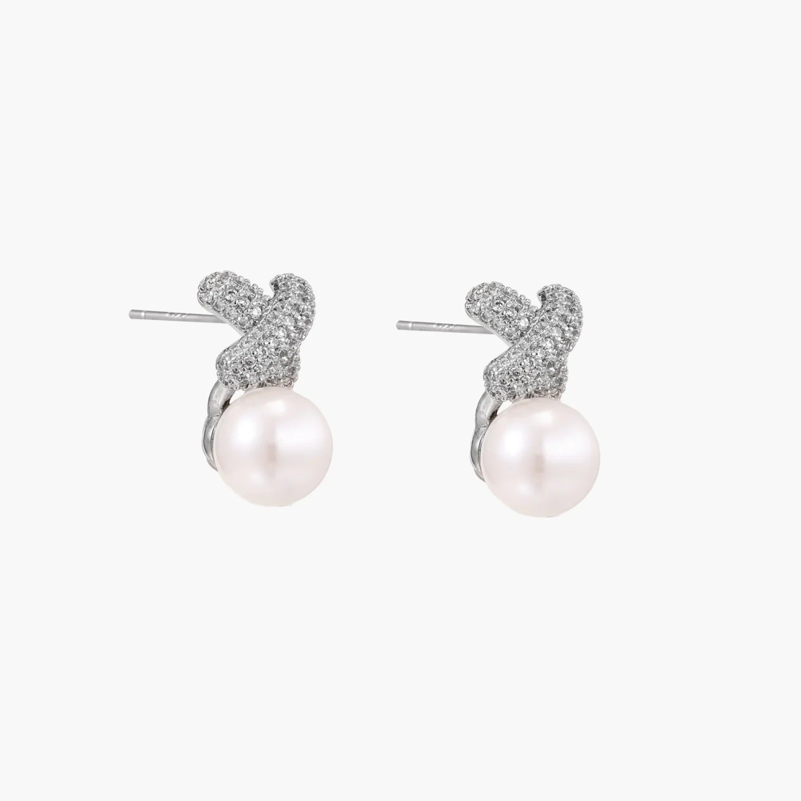 White gold plated studs featuring pavé X-shaped tops with freshwater pearl drops on cream background.