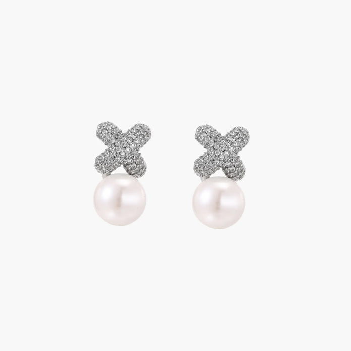 White gold plated studs featuring pavé X-shaped tops with freshwater pearl drops on cream background.