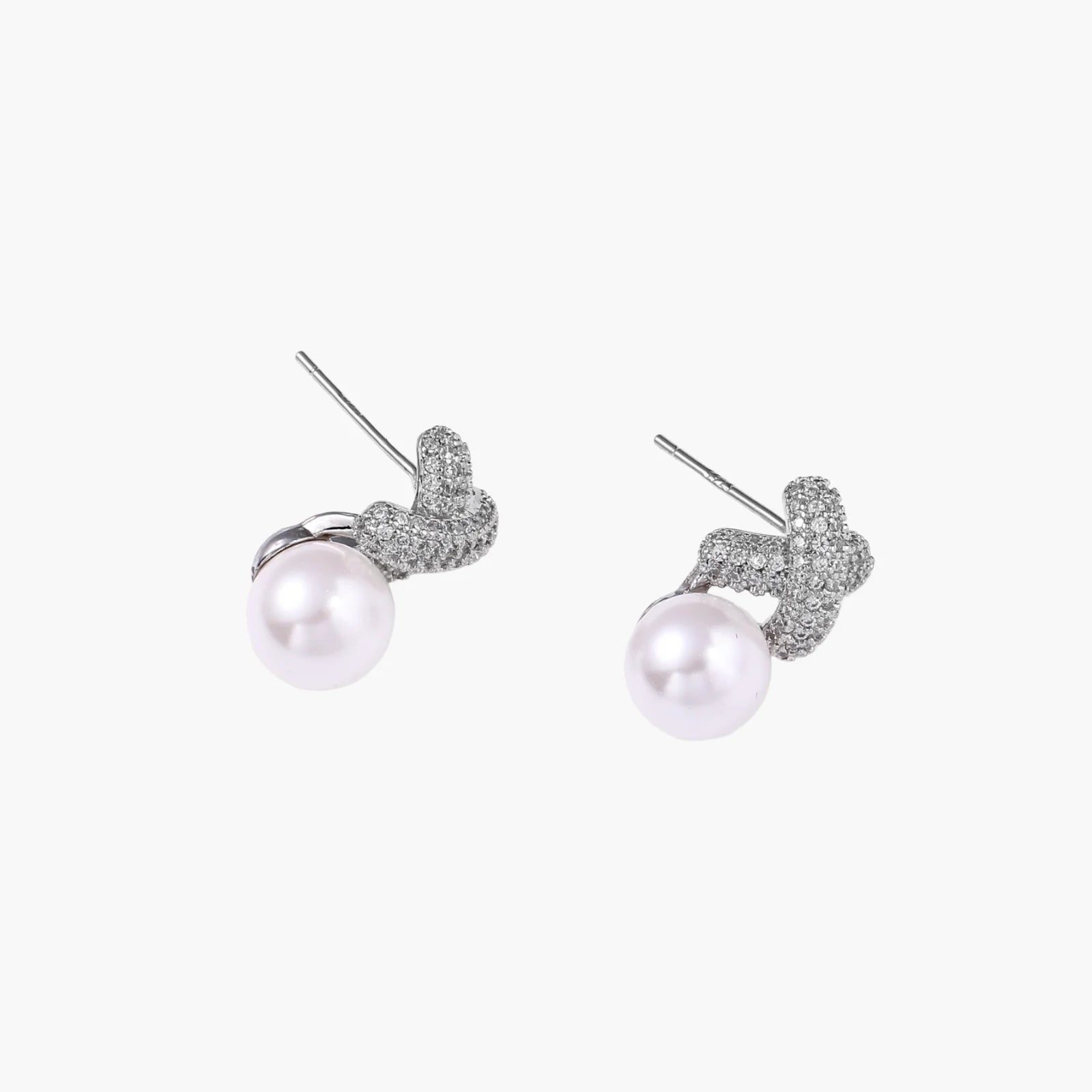 White gold plated studs featuring pavé X-shaped tops with freshwater pearl drops on cream background.