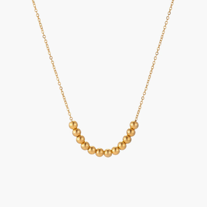 Delicate gold-plated necklace with graduated spherical beads forming gentle smile curve on beige background
