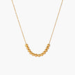 Delicate gold-plated necklace with graduated spherical beads forming gentle smile curve on beige background