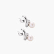 Rhodium-plated silver earrings with twisted X design and freshwater pearl drops on beige background