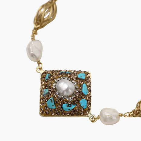 Gold-plated bracelet with baroque centerpiece, turquoise stones, freshwater pearls, and ornate chain links on cream background.