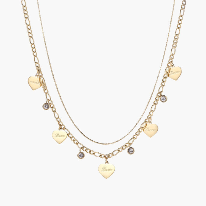 Gold layered necklace set with engraved heart pendants and crystal accents on cream background