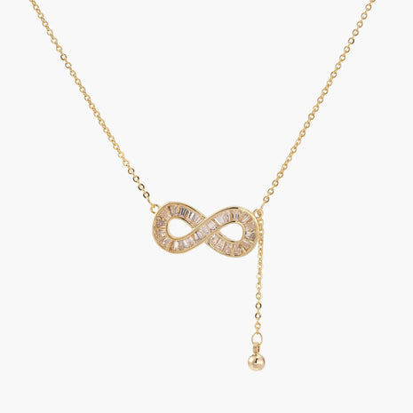 Gold infinity pendant with baguette crystals on adjustable chain against cream background.