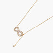 Gold infinity pendant with baguette crystals on adjustable chain against cream background.
