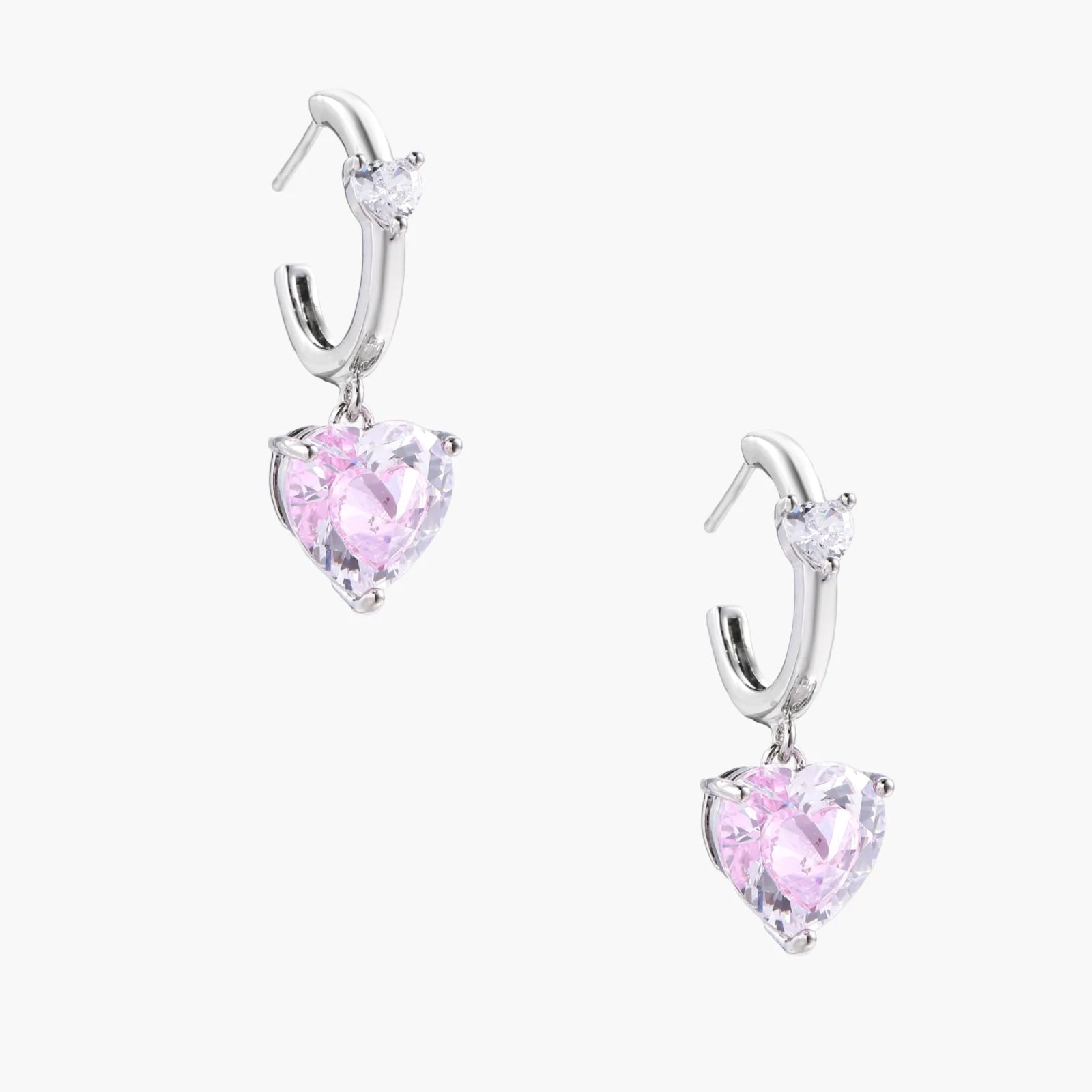 Silver huggie hoops with pink heart-cut zirconia pendants on white background, eco-friendly white gold plated brass
