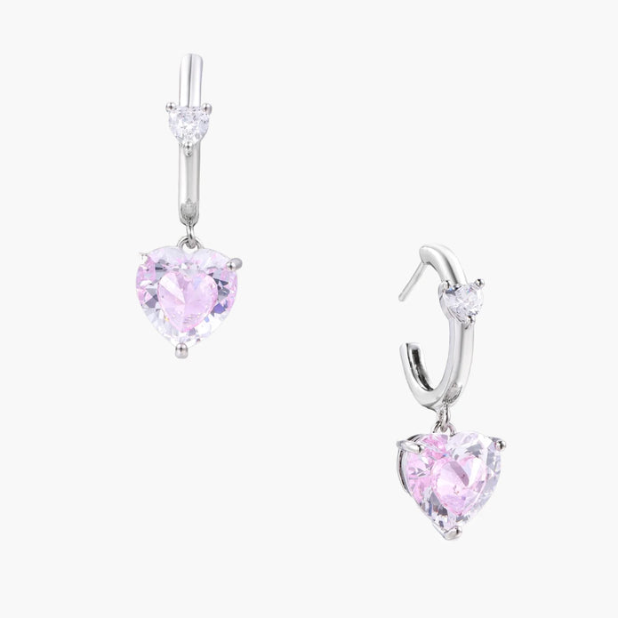 Silver huggie hoops with pink heart-cut zirconia pendants on white background, eco-friendly white gold plated brass