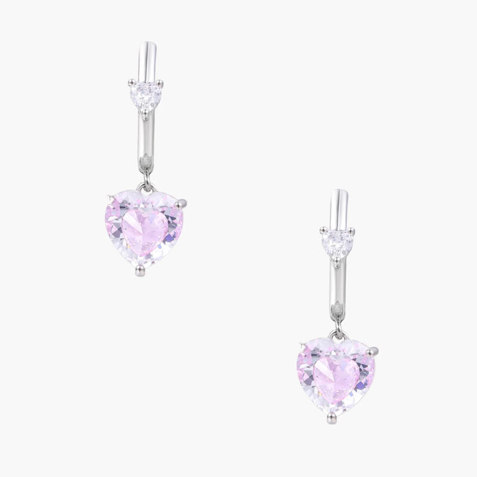 Silver huggie hoops with pink heart-cut zirconia pendants on white background, eco-friendly white gold plated brass