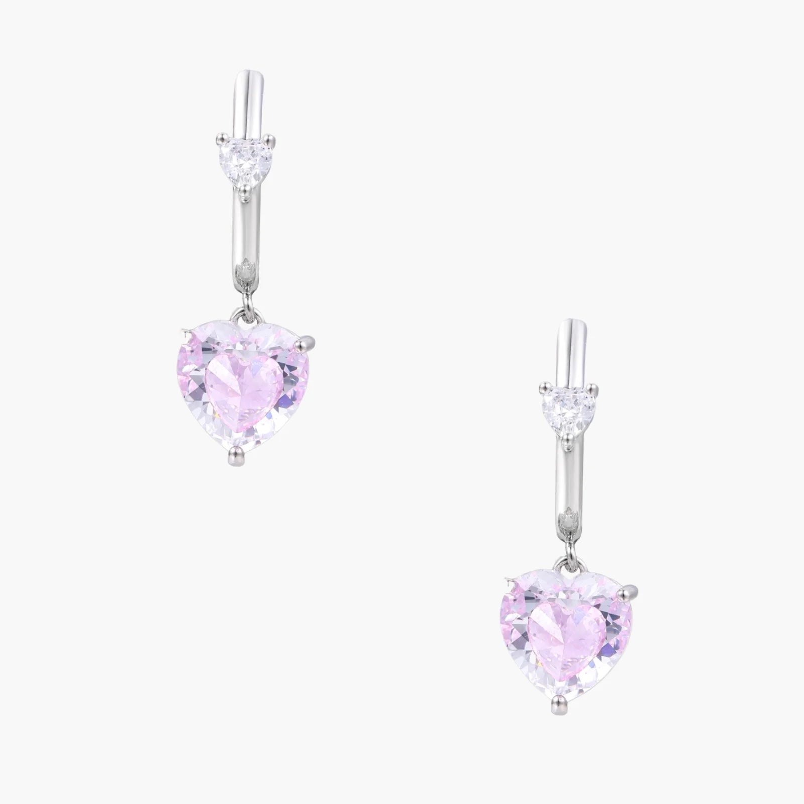 Silver huggie hoops with pink heart-cut zirconia pendants on white background, eco-friendly white gold plated brass