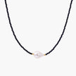 Delicate necklace with black blue sandstone beads and baroque pearl center on white background with gold accents.