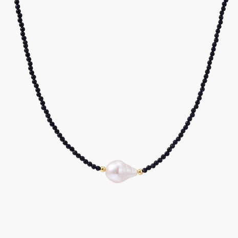 Delicate necklace with black blue sandstone beads and baroque pearl center on white background with gold accents.