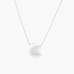 Minimalist brushed sterling silver dome pendant on delicate chain against cream background, showing matte textured finish