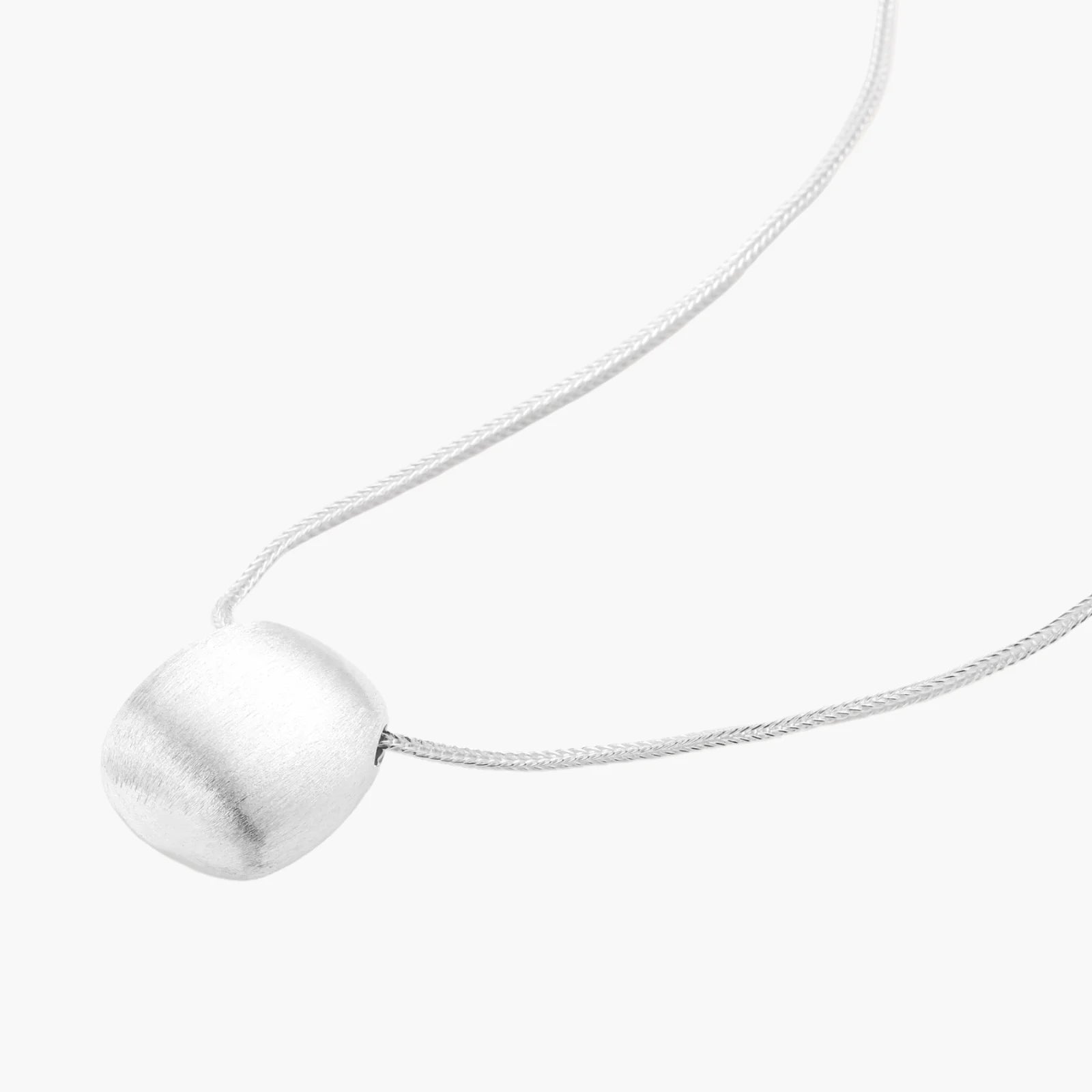Minimalist brushed sterling silver dome pendant on delicate chain against cream background, showing matte textured finish