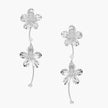 Silver-white asymmetric earrings with textured flower petals and crystal centers on cream background