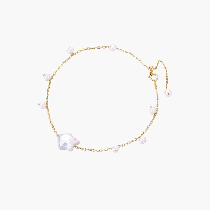 Delicate gold chain bracelet with baroque pearl centerpiece and small freshwater pearls on cream background.