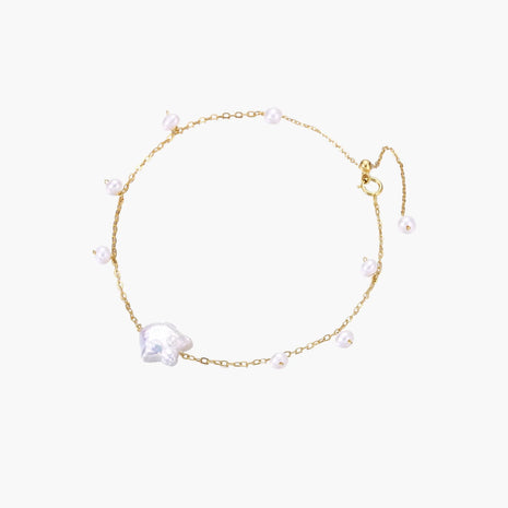 Delicate gold chain bracelet with baroque pearl centerpiece and small freshwater pearls on cream background.