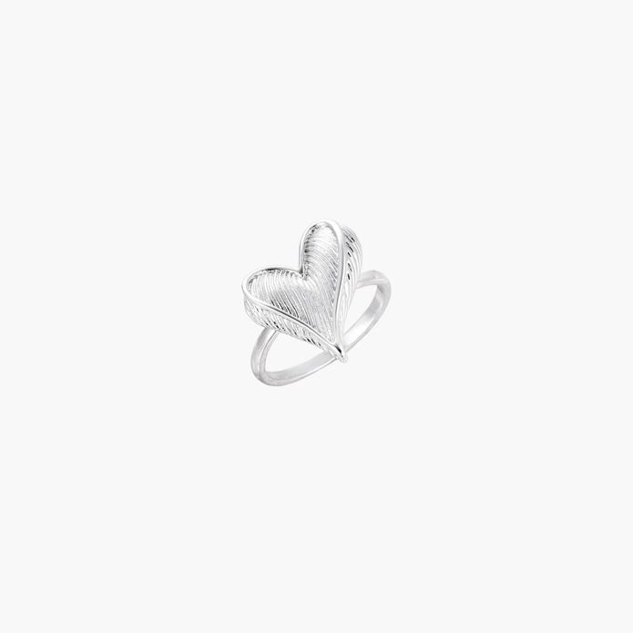 Silver ring with 3D heart formed by textured feather-like elements, white gold plated eco-brass on neutral background.