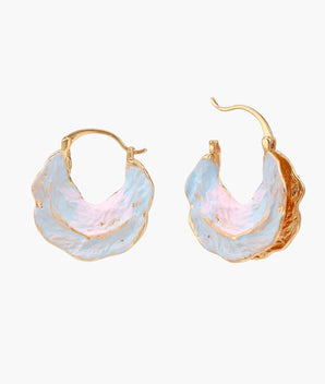 Shell-shaped hoop earrings with iridescent blue-pink enamel and gold trim on cream background