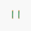 Pair of small gold huggie hoop earrings with bright green cubic zirconia stones on cream background