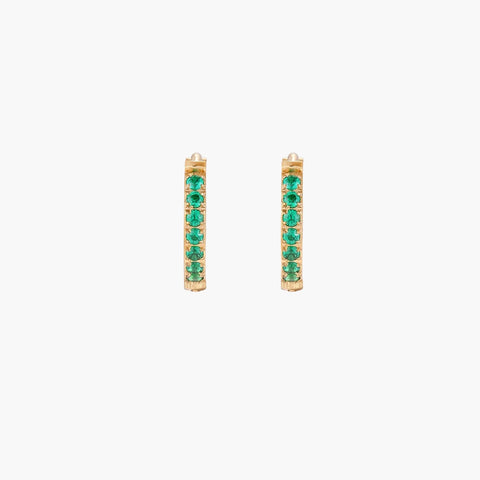 Pair of small gold huggie hoop earrings with bright green cubic zirconia stones on cream background