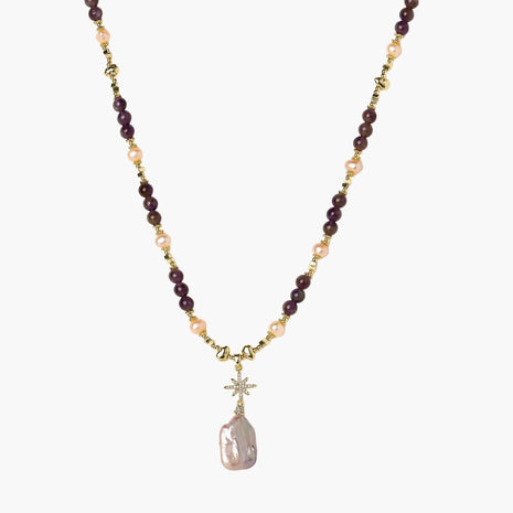 Gold necklace with iridescent baroque pearl pendant, purple amethyst beads, and crystal star charm on cream background