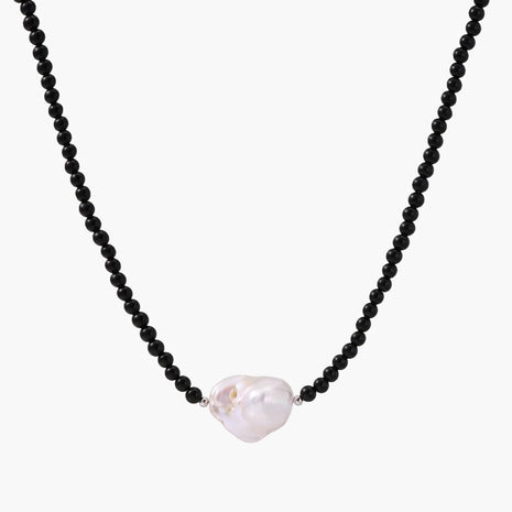 Beaded black agate necklace with iridescent baroque freshwater pearl centerpiece on cream background.