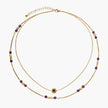 Two layered gold-tone necklaces with purple stone beads and star pendant against cream background.