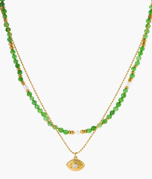 Layered necklace with green stone beads, gold spacers, white accents, and protective eye pendant on cream background.