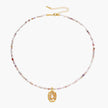 Delicate gold-plated necklace with mixed gemstone beads and ornate oval pendant on white background
