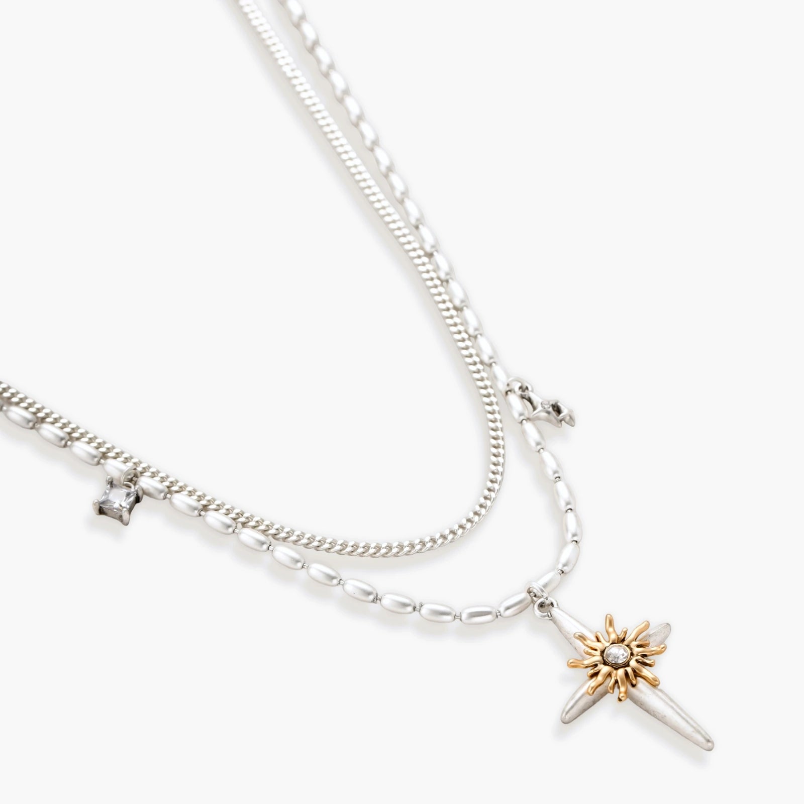 Two-layer silver-toned necklace with star charms and dagger pendant featuring golden sun motif on white background.