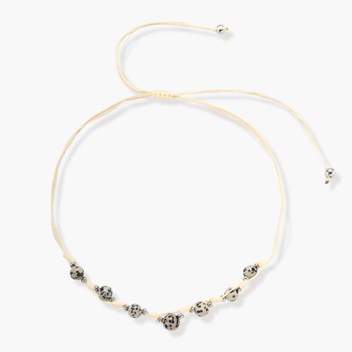 Adjustable cream cord necklace with white spotted stone beads featuring black speckles on neutral background