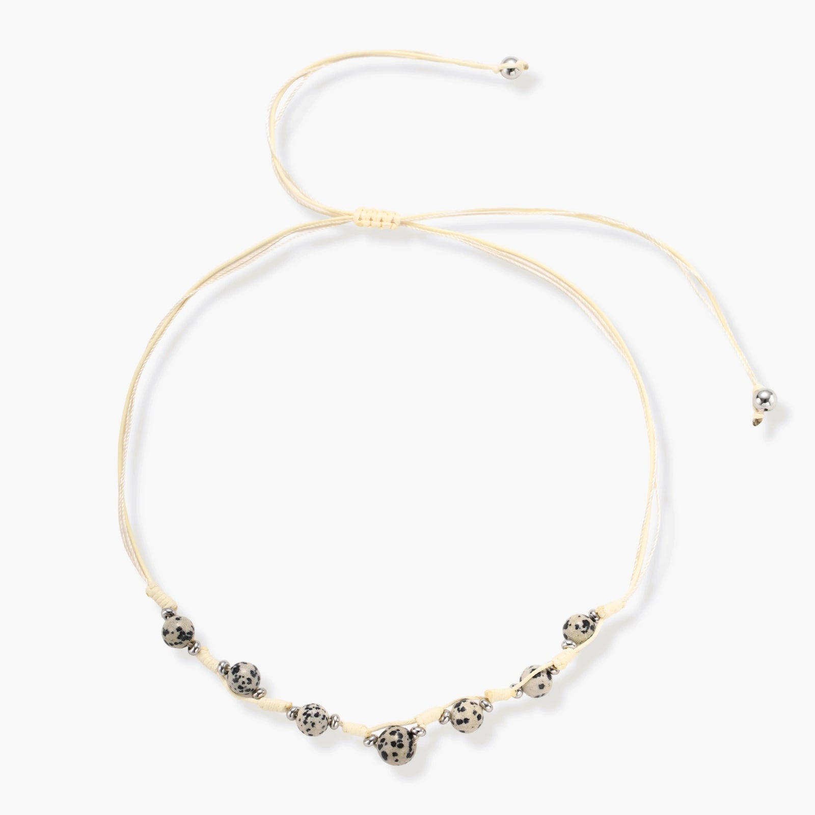 Adjustable cream cord necklace with white spotted stone beads featuring black speckles on neutral background
