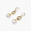 Gold sunburst charm earrings with baroque pearl drops on French hooks against cream background