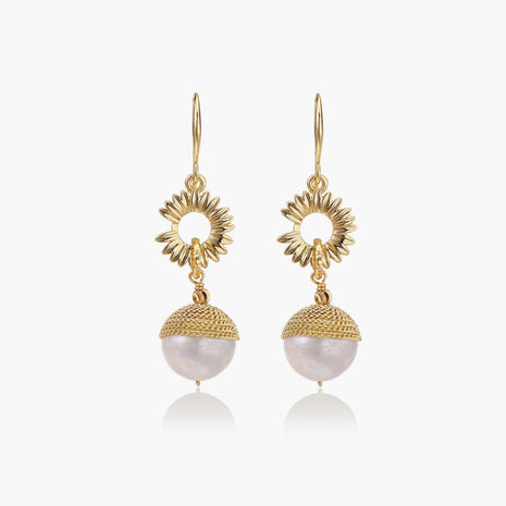 Gold sunburst charm earrings with baroque pearl drops on French hooks against cream background