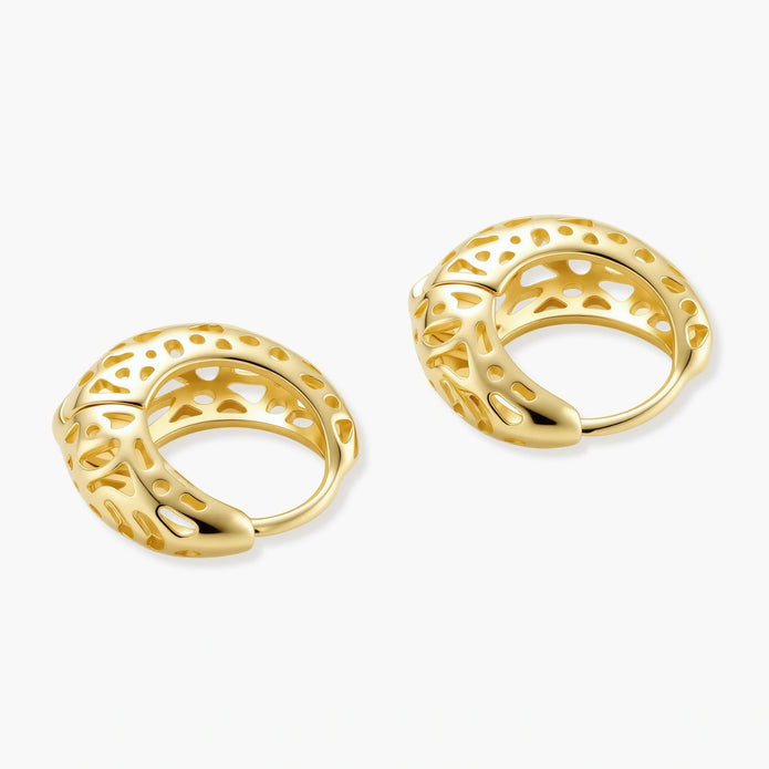 Close-up of small gold-plated hoop earrings with intricate honeycomb cutout pattern on cream background.