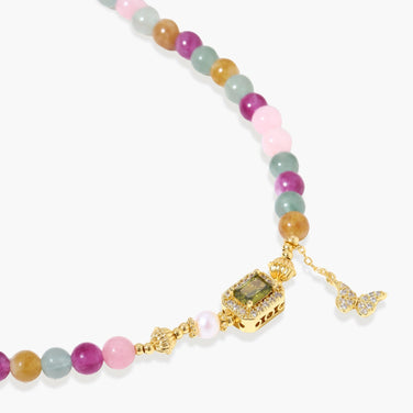 Stretchable bracelet with pastel gemstone beads, freshwater pearls, gold centerpiece and butterfly charm on cream background