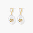 Gold-plated drop earrings with iridescent baroque pearls and crystal flower accents on cream background