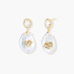 Gold-plated drop earrings with iridescent baroque pearls and crystal flower accents on cream background