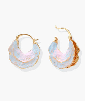 Shell-shaped hoop earrings with iridescent blue-pink enamel and gold trim on cream background