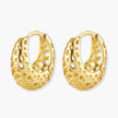 Close-up of small gold-plated hoop earrings with intricate honeycomb cutout pattern on cream background.