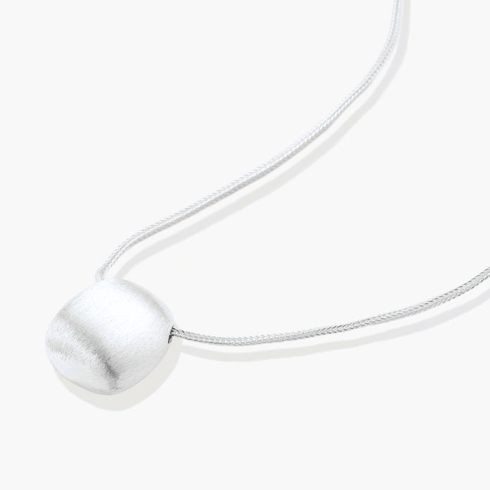 Minimalist brushed sterling silver dome pendant on delicate chain against cream background, showing matte textured finish