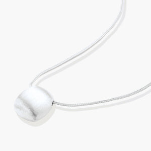 Minimalist brushed sterling silver dome pendant on delicate chain against cream background, showing matte textured finish