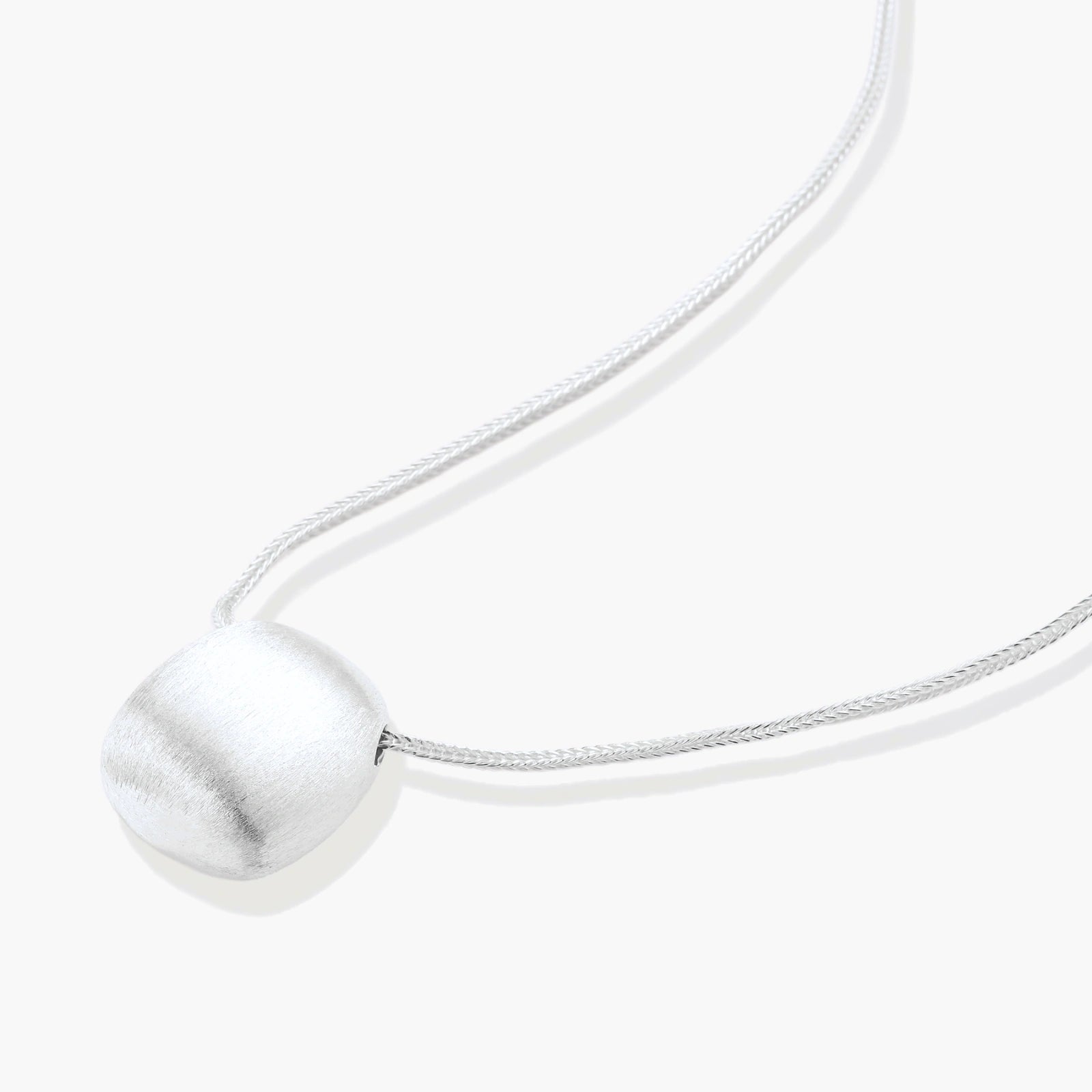 Minimalist brushed sterling silver dome pendant on delicate chain against cream background, showing matte textured finish